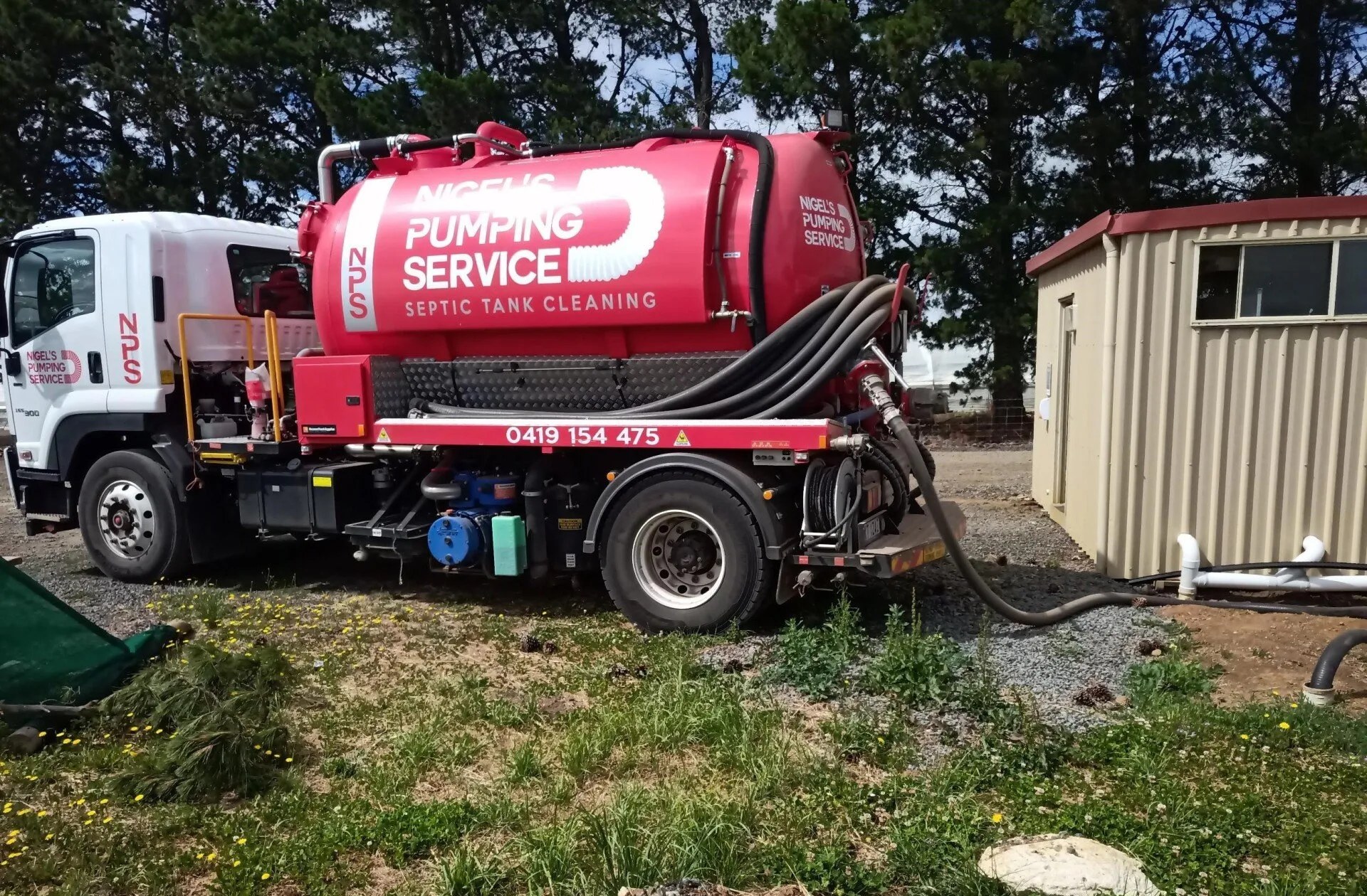 The Nigel's Pumping Service tanker with suction hoses unspooled beside a site shed during a septic tank cleaning
