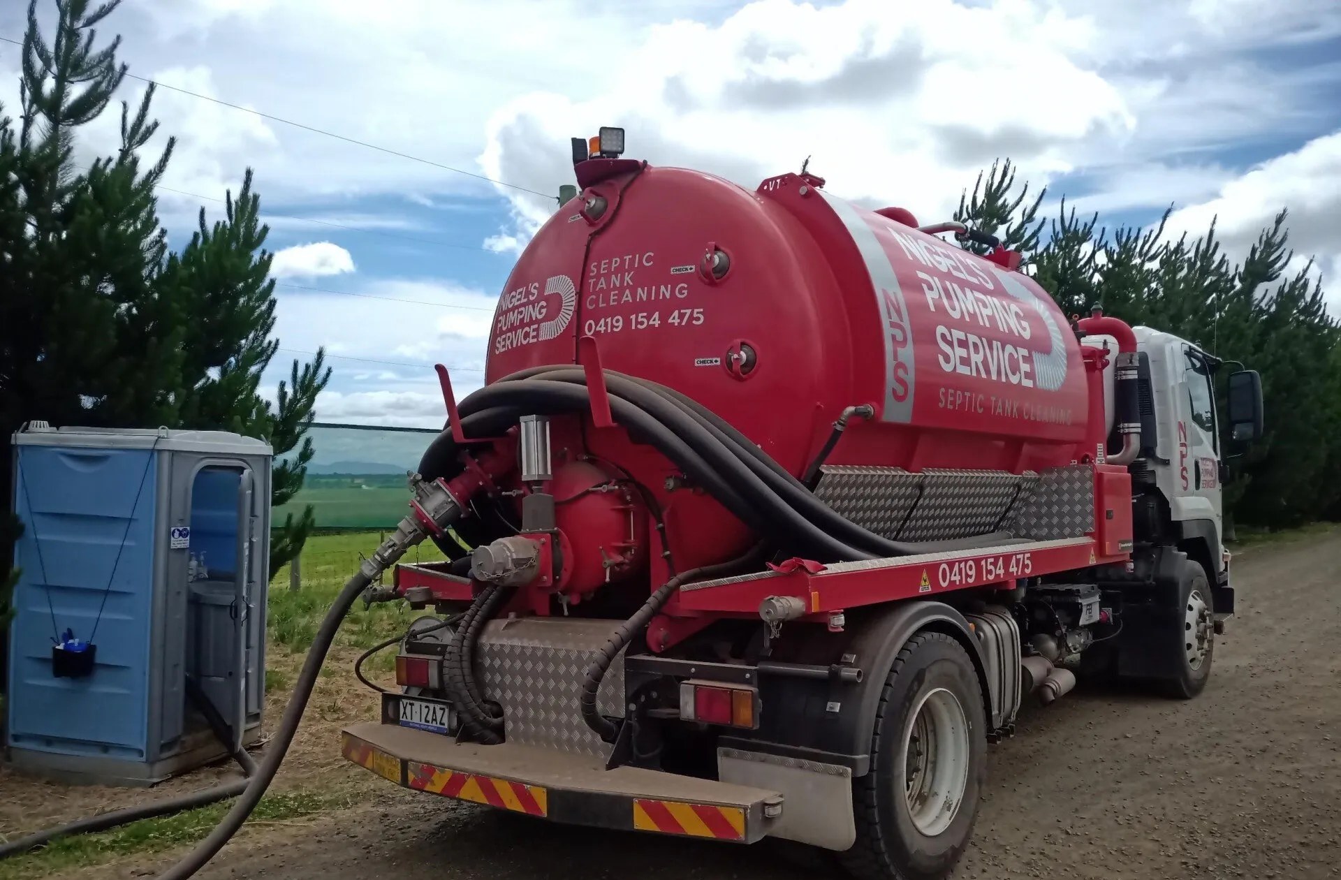 Nigel's Pumping Service red vacuum tanker with the suction hose connected to a portaloo on a Launceston property