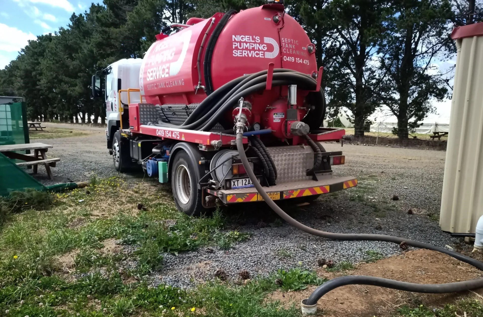 Vacuum hose lowered into a septic tank access point during a pump-out on a grassy Launceston block